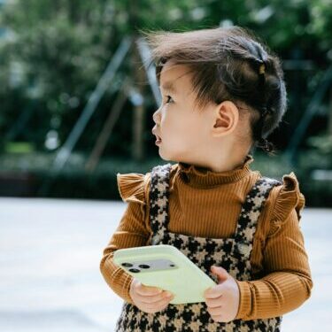 A young child holding a light green smartphone.