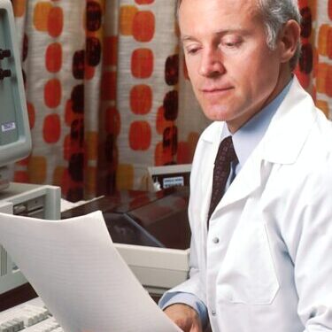 Photo by National Cancer Institute man reading papers in front of computer