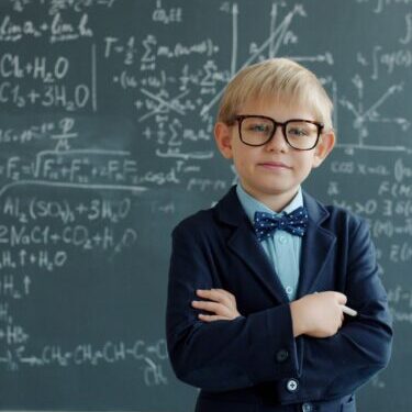 vitaly-gariev-PGagGdu0Vec-unsplash smart kid in a suit jacket, bow tie, and glasses in front of a chalkboard with scientific writing